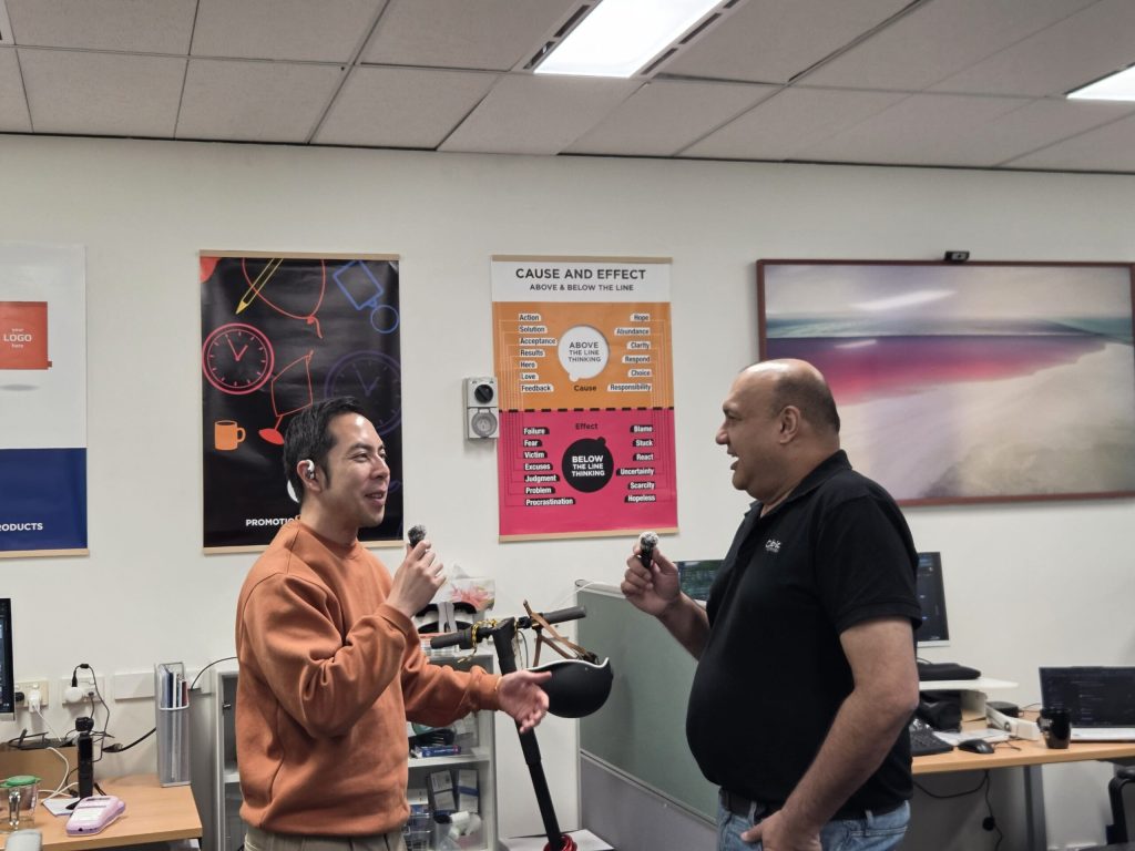 Two men smiling and talking with microphones discuss employee appreciation in the office.