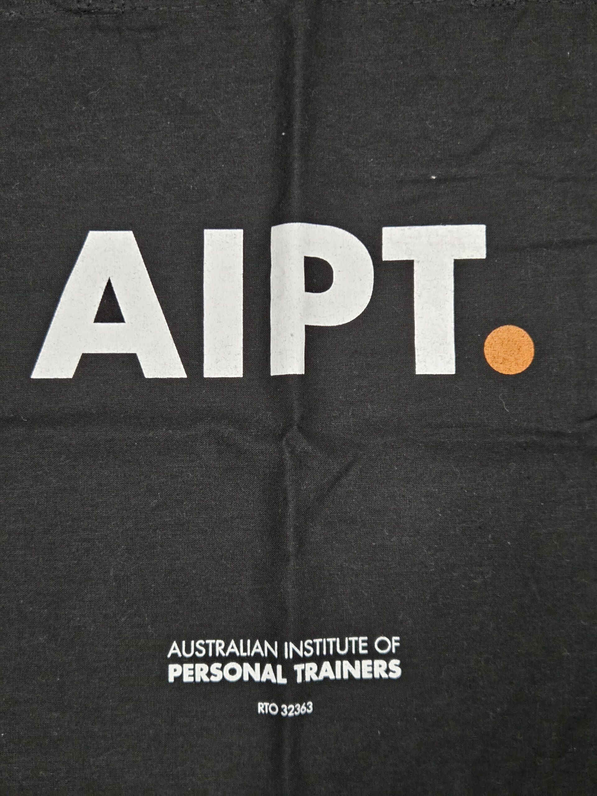 Black fabric with AIPT. in bold white, worn proudly by a happy client of the Institute.
