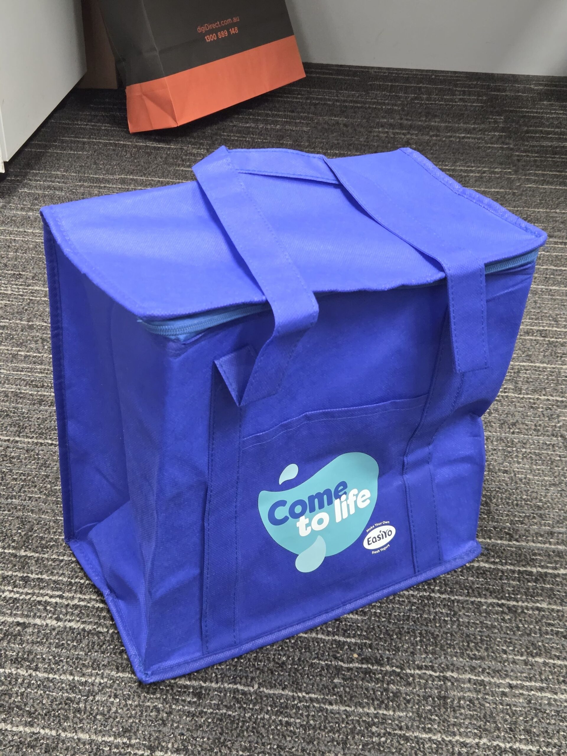 A blue EasiYo reusable bag with Come to life printed on the front, sitting on carpet.