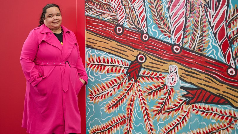 Woman in a bright pink coat stands by a mural inspired by Aboriginal Artists and red patterns.