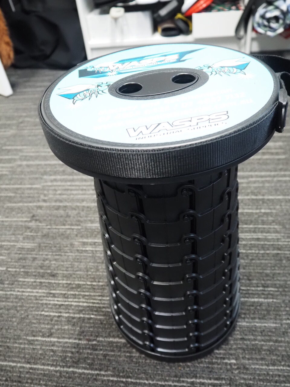 Black and blue collapsible bucket from WASPS, with strap, on a gray carpeted floor.