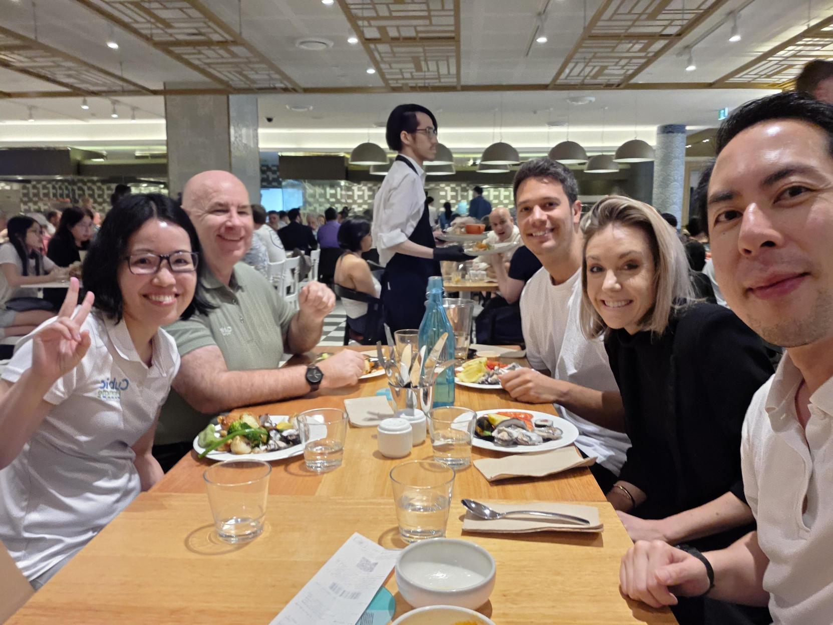 Five people smiling and dining together on a holiday break, plates of food on the table.