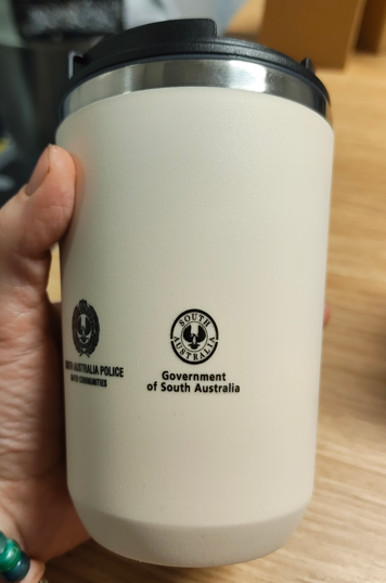 A hand holds a white tumbler with the SA Police and Government of South Australia logos.