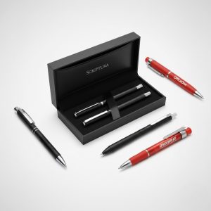 Five promotional pens: two in a black Scriptura box, three loose on a white surface.