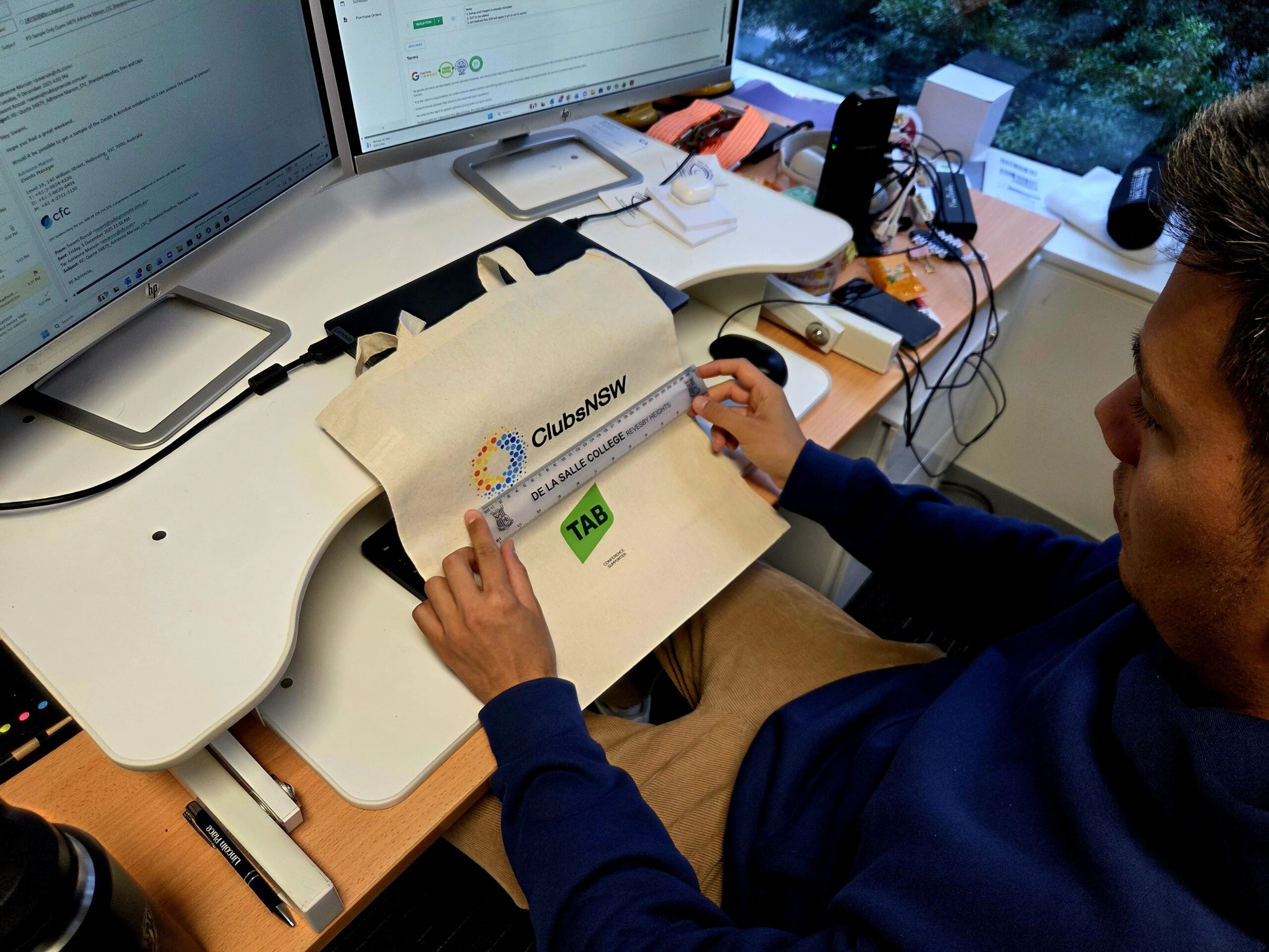 A day in the life: Measuring a ClubsNSW tote bag from Cubic Promote at an office desk.