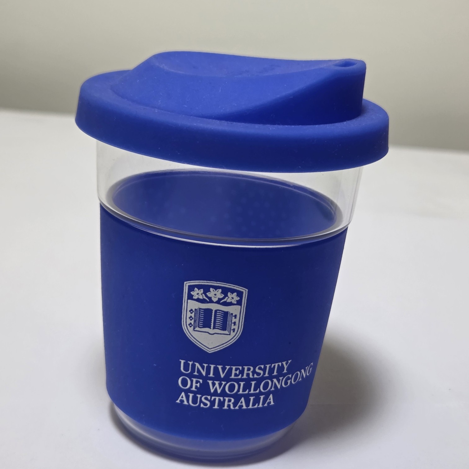 Blue reusable cup in University of Wollongong branding colours on a white surface.