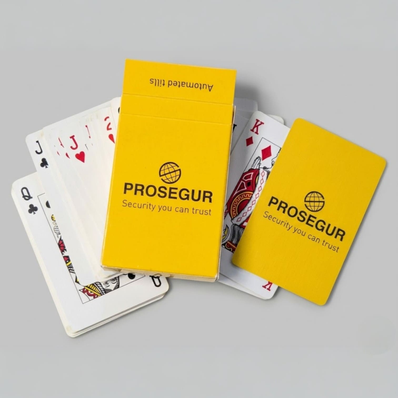 A yellow Prosegur Promo Packs playing card box with scattered cards on a gray surface.