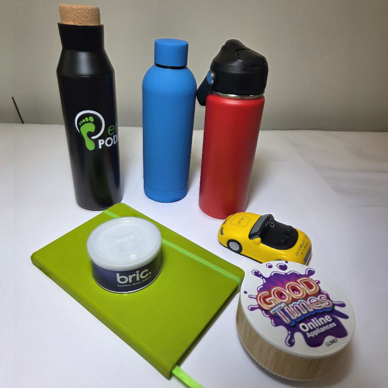 Three bottles, a green notebook in branding colours, toy car, and two round containers on white.
