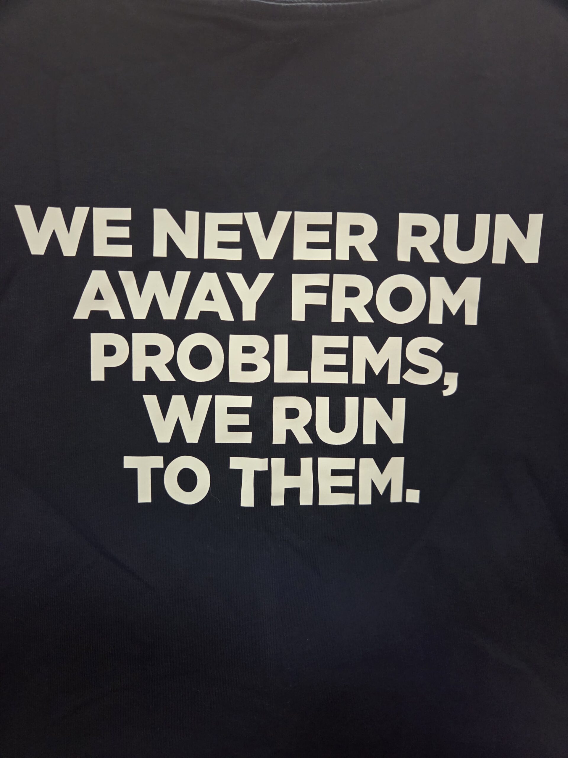 Text on shirt: We never run away from problems, we run to them—embroidery vs screen printing style.