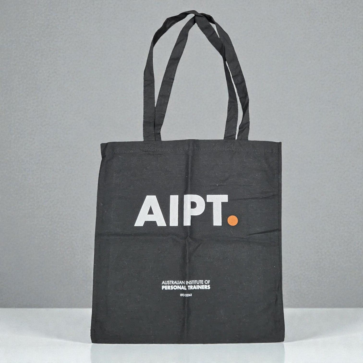 A black tote bag with AIPT. printed in white and orange, ensuring print colour accuracy.