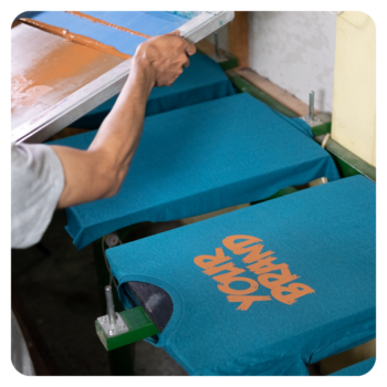 A person screen-printing YOUR BRAND on durable golf shirts in blue with orange ink.
