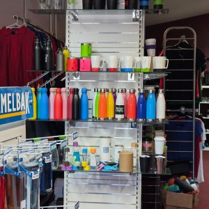 Display of colorful promotional products like reusable bottles, mugs, and tumblers on shelves.