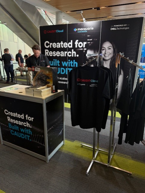 Exhibition booth with CAUDITCloud branding, t-shirts, and Macquarie Cloud Services materials on display.