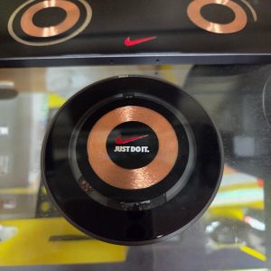 Round wireless charging pad with copper coil, Nike logo, and quality products slogan visible.