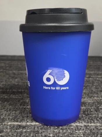 Blue reusable cup with black lid; ideal for bulk orders to avoid delays. 60 Here for 60 years.