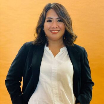 Meet the team: Woman in a black blazer and white blouse smiling before an orange background.