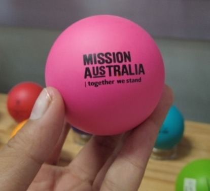 Hand holding a pink ball labeled Mission Australia; printing process ensures materials compatibility.