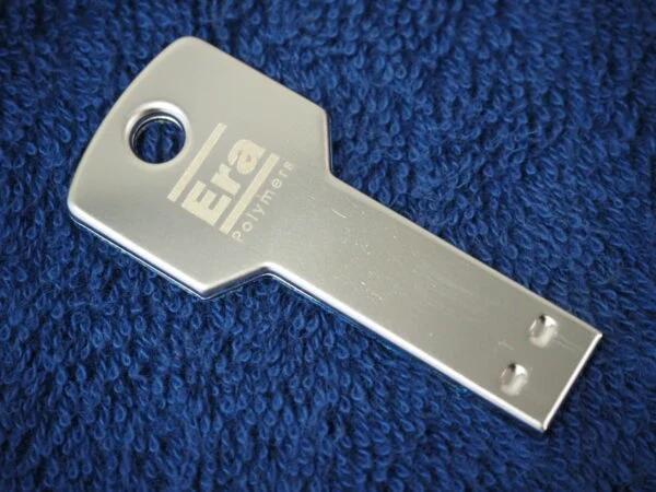 Silver cap USB drive shaped like a key, placed on a blue textured fabric background.