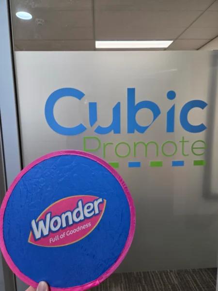 A hand holds a blue Wonder frisbee, perfect for logo file formats like EPS or PDF, by the glass door.