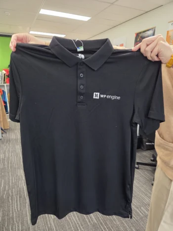 A person holds a black WP Engine polo shirt featuring an EPS logo, ideal for printing.