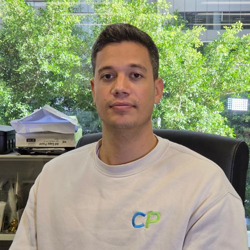 Meet the team: A man in a white sweatshirt sits in an office with trees visible behind him.